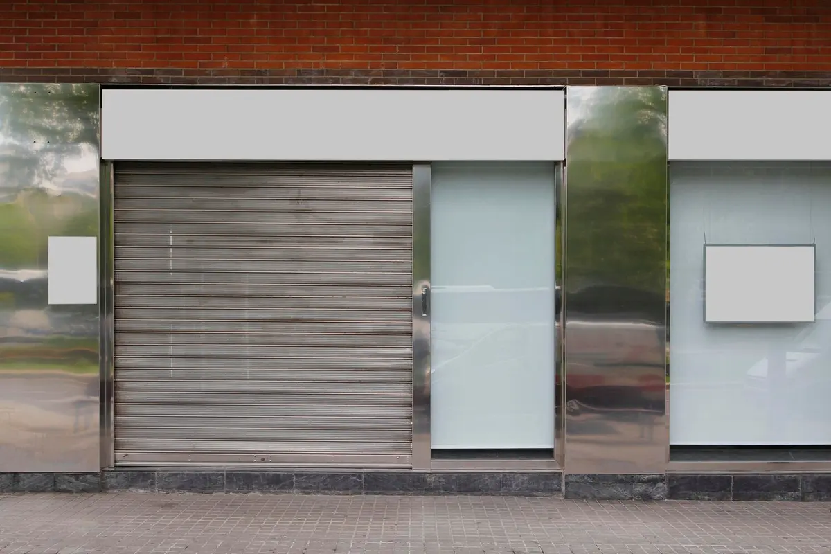 Rideau métallique baissé devant l'entrée d'une boutique à vitrines dépolies et encadrements en inox