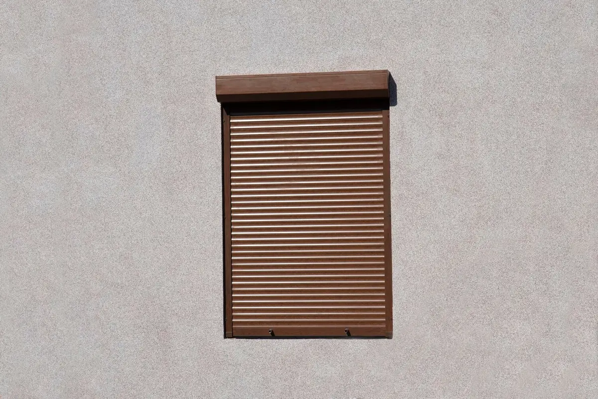 Volet roulant marron baissé, coffre extérieur posé au-dessus de la fenêtre, sur une façade crépie